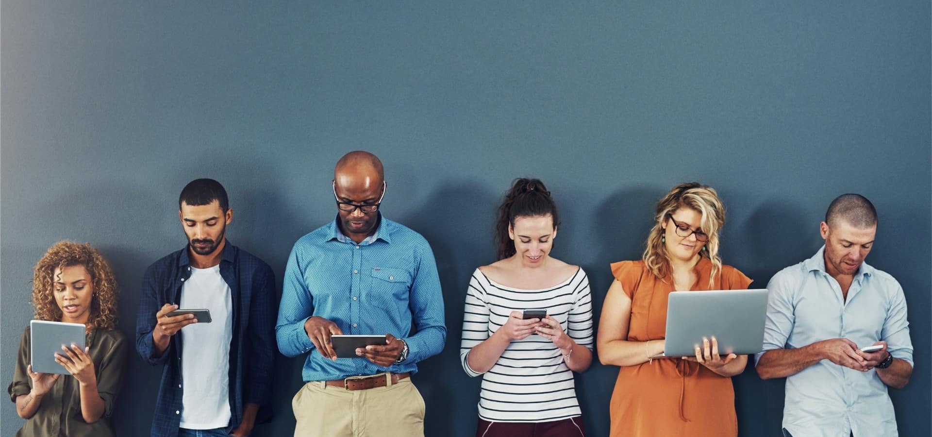 A group of people distracted due to the overuse of technology against gray studio background