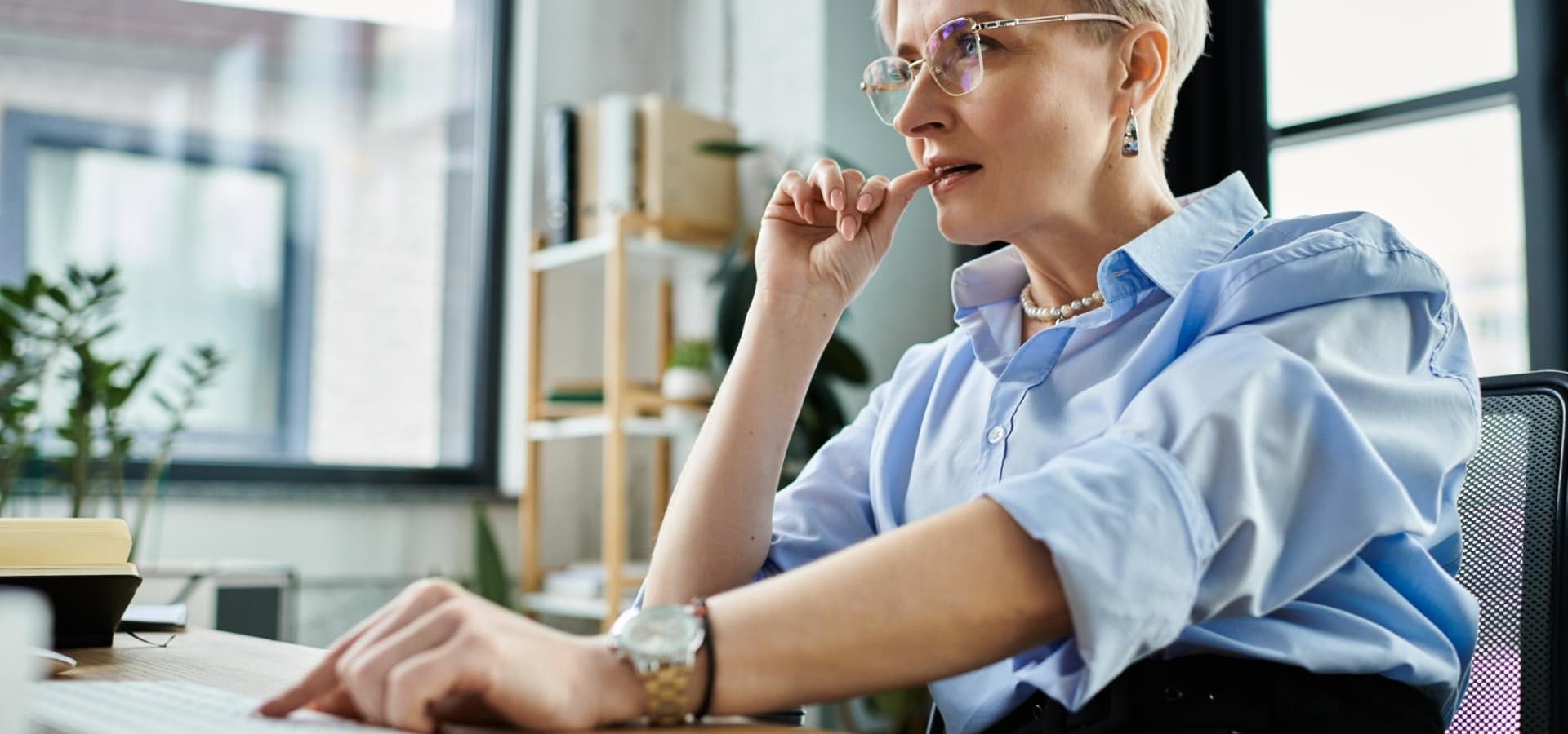 A middle aged businesswoman with short hair concentrates on work tasks using a laptop computer in an office setting