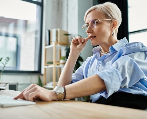 A middle aged businesswoman with short hair concentrates on work tasks using a laptop computer in an office setting