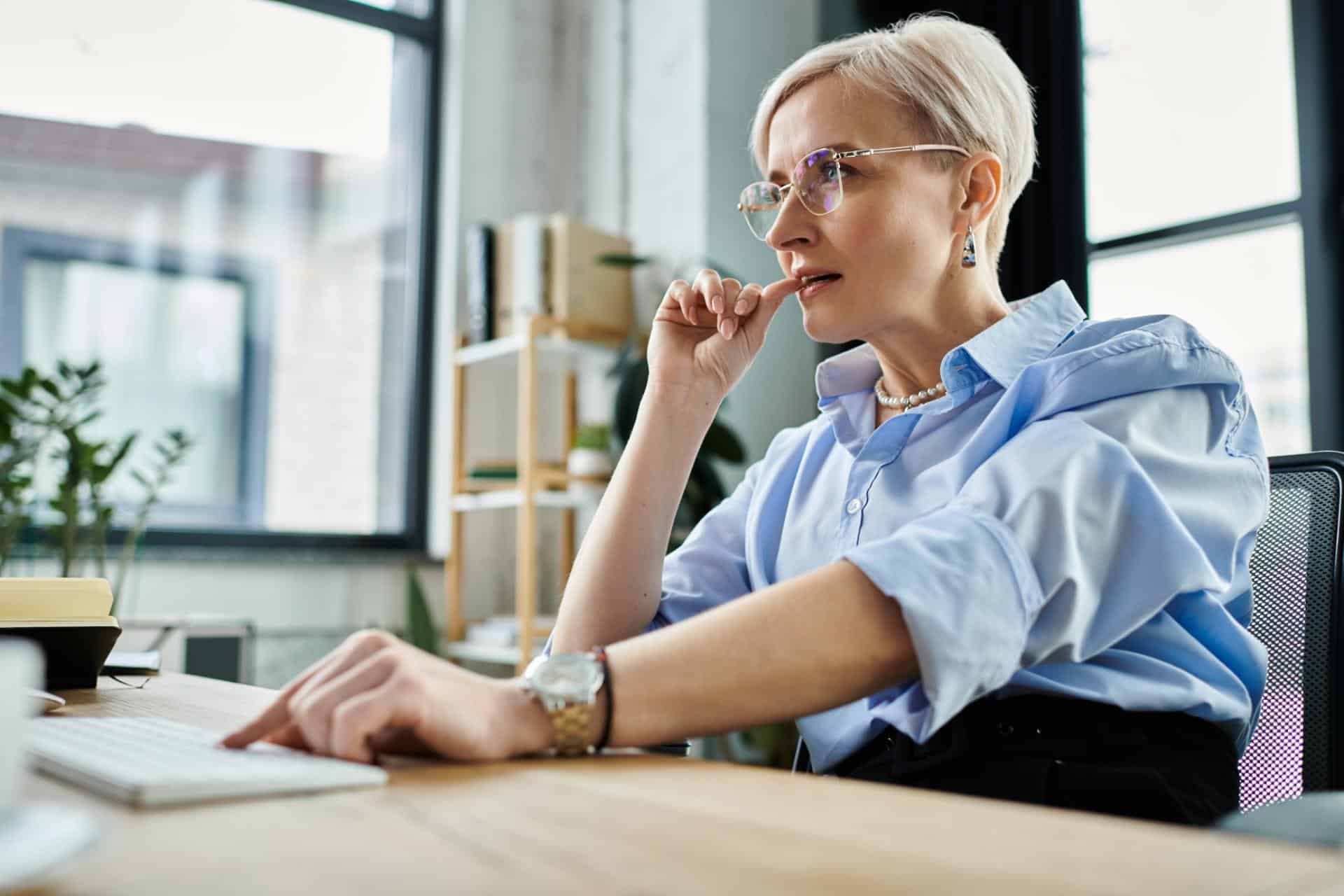 A middle aged businesswoman with short hair concentrates on work tasks using a laptop computer in an office setting