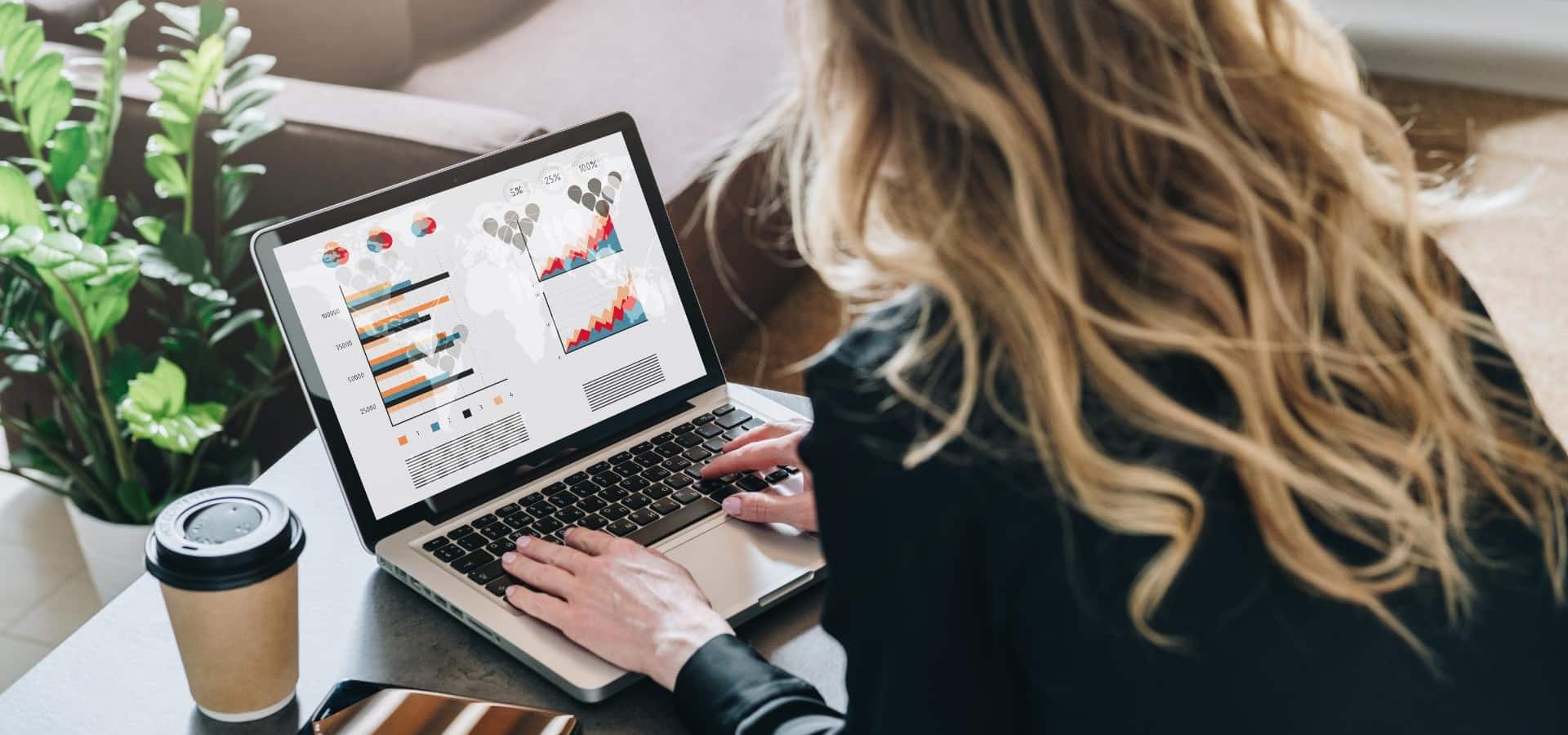 Rear view Young businesswoman is sitting at table working on laptop with graphs