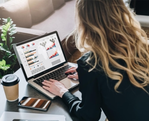 Rear view Young businesswoman is sitting at table working on laptop with graphs