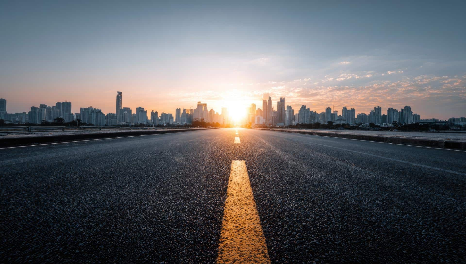 Empty asphalt road leading to a city skyline at sunrise